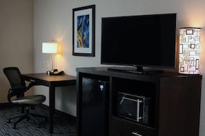 A hotel room with a desk, chair, television, refrigerator, and a lamp. - Holiday Inn Express & Suites Omaha South - Ralston Arena by IHG (Omaha)