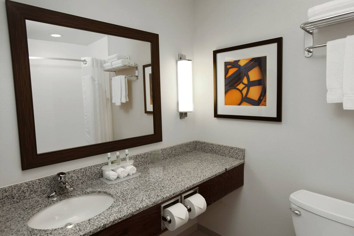 A bathroom with a granite countertop sink, a large mirror, a framed abstract painting, and a toilet.