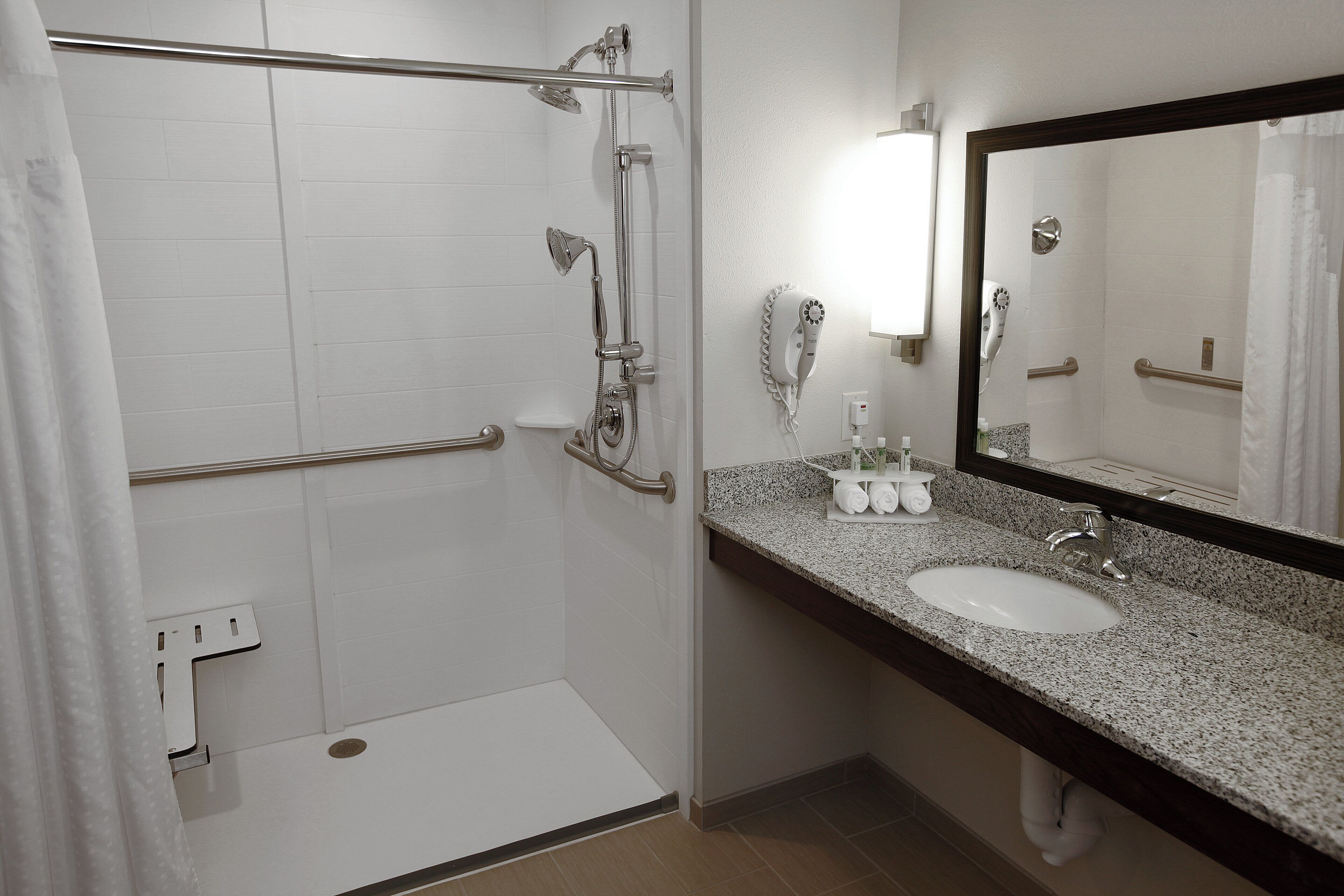 A bathroom with a shower, a sink, a mirror, and a towel rack.