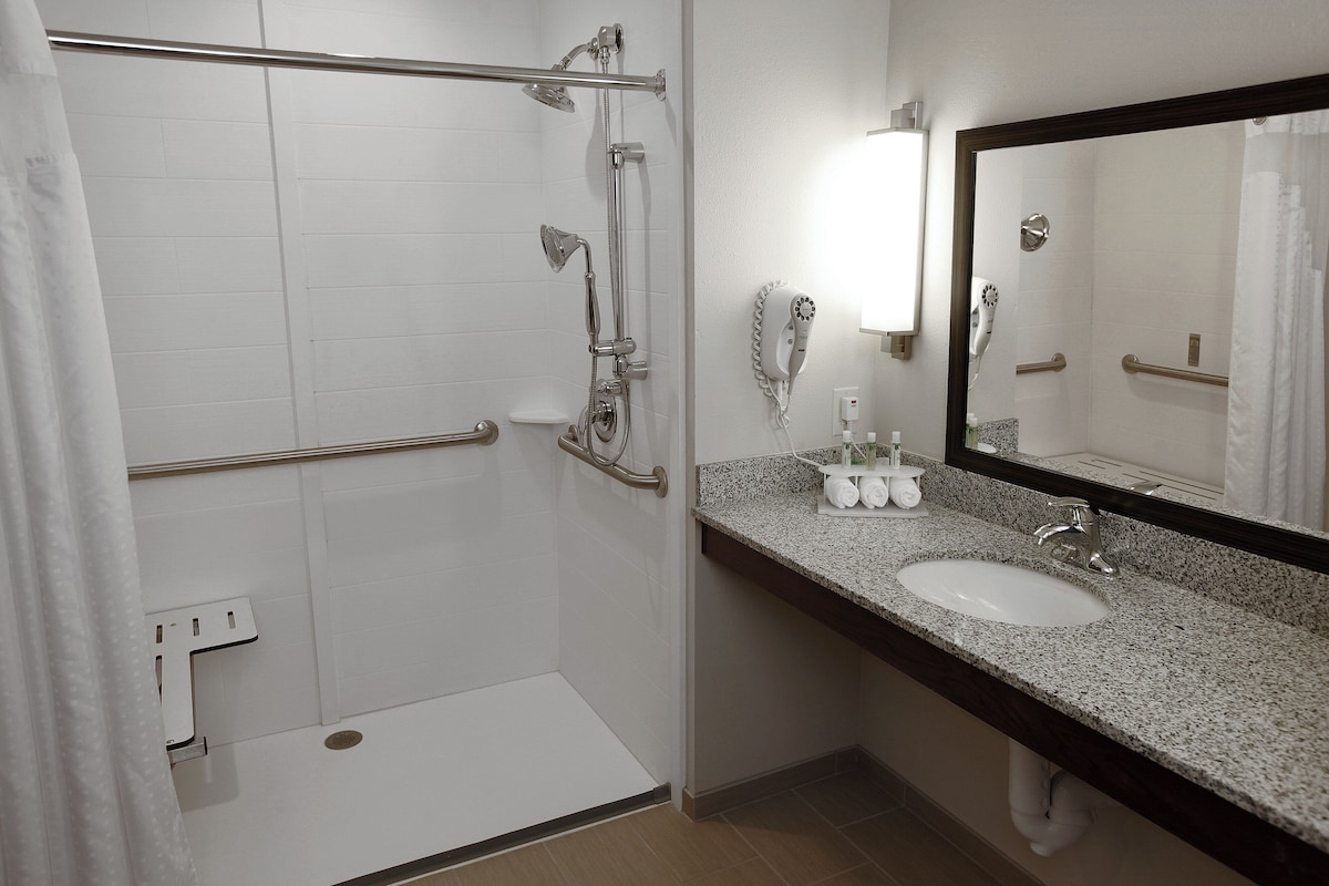 A bathroom with a shower, a sink, a mirror, and a towel rack.