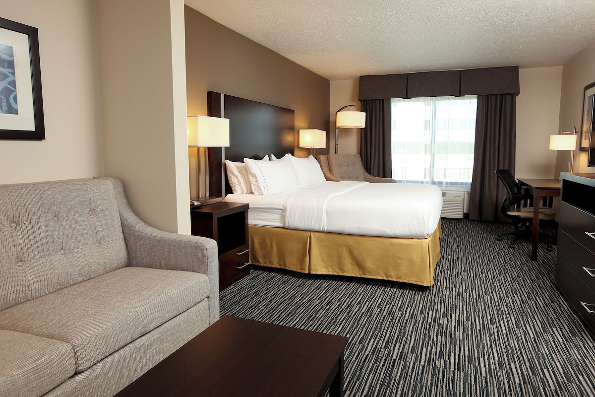 A hotel room with a bed, a sofa, a desk, and a television.