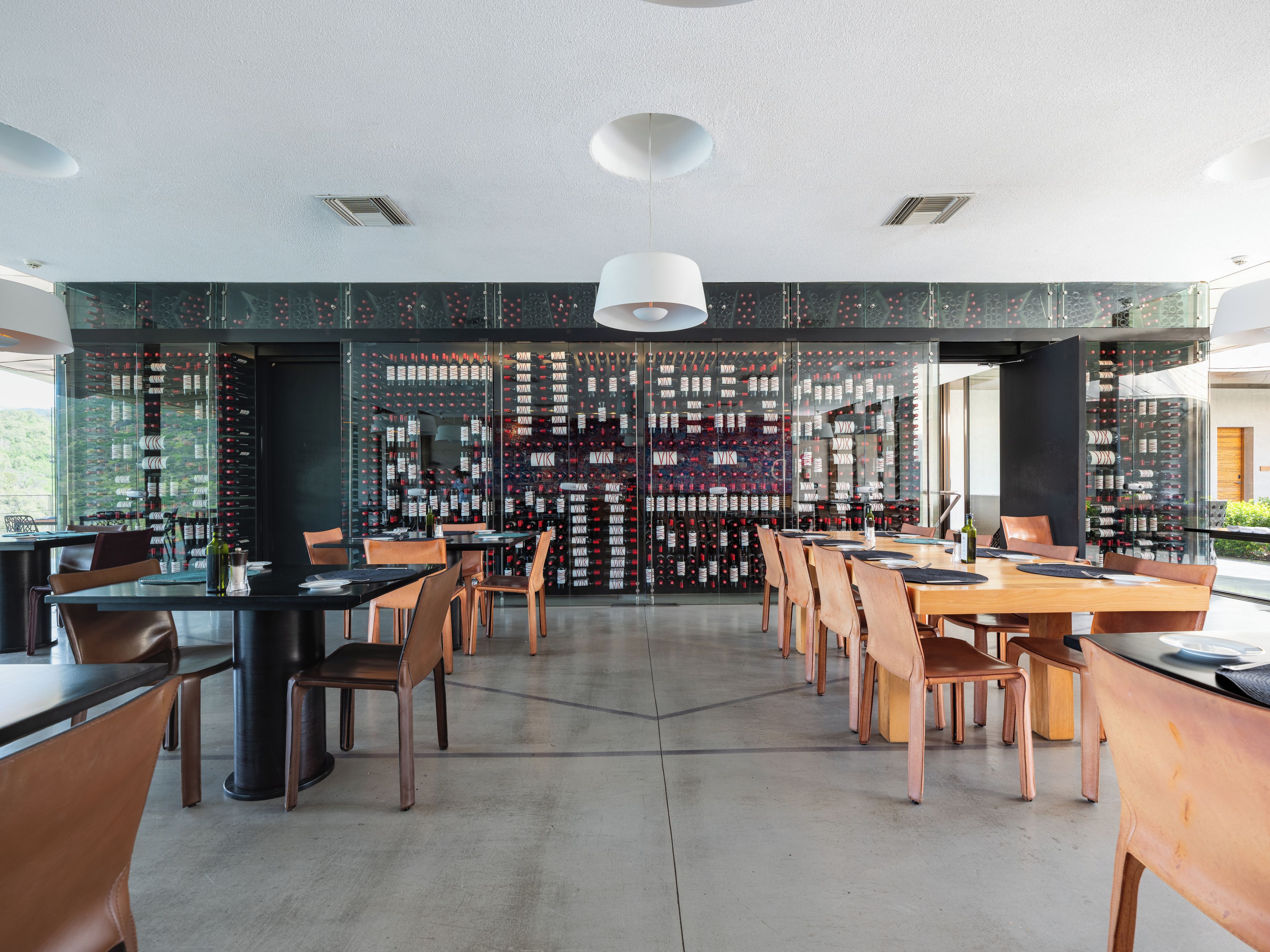 Un restaurant moderne doté d’une cave à vin visible à travers des murs de verre, où sont exposées de nombreuses bouteilles de vin.