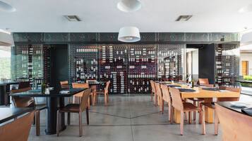 Un restaurant moderne doté d’une cave à vin visible à travers des murs de verre, où sont exposées de nombreuses bouteilles de vin.