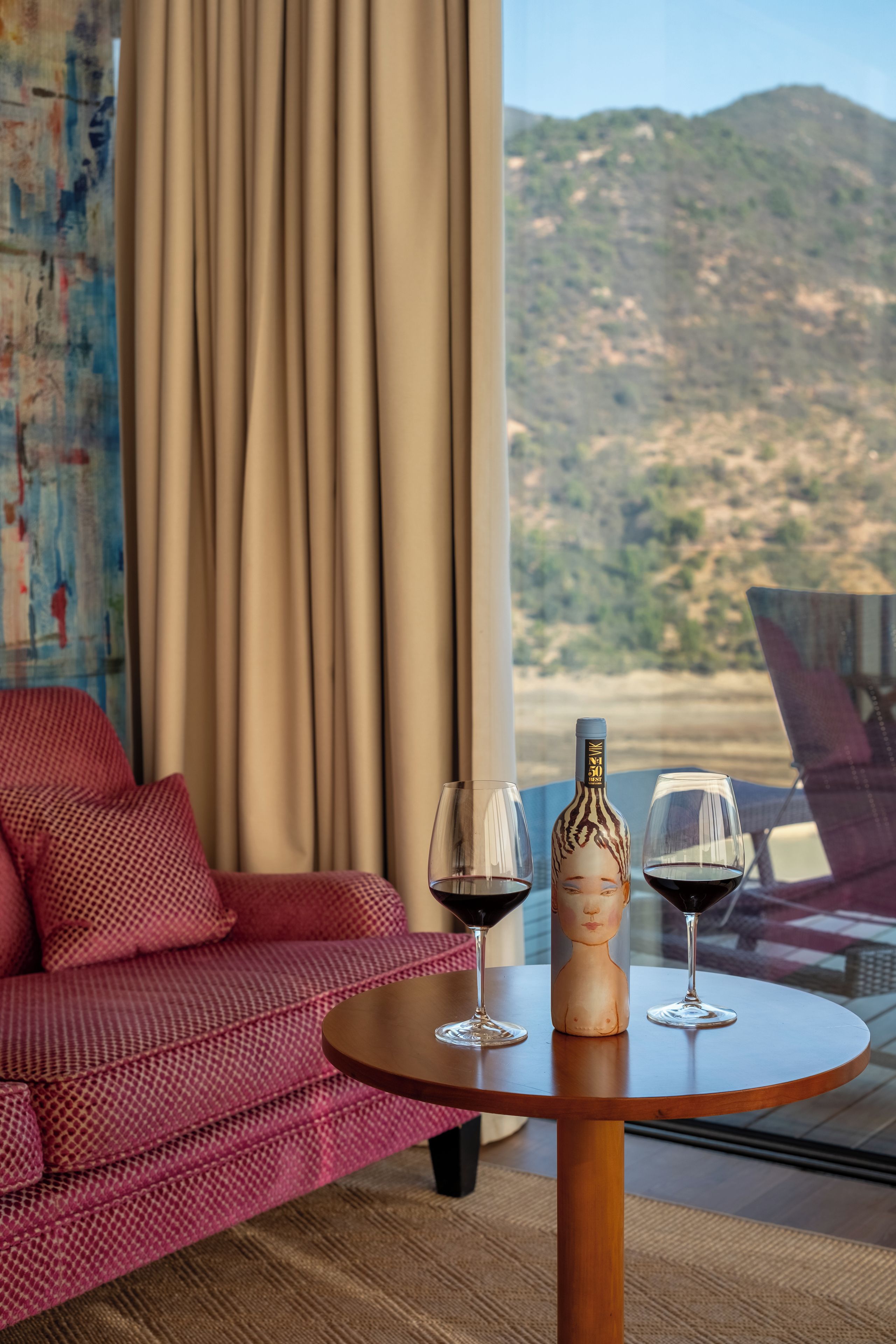 Una habitación con una mesa redonda, dos copas de vino y una botella, con vista a las montañas a través de una ventana.