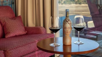 A room with a round table, two wine glasses, and a bottle, with a view of mountains through a window.