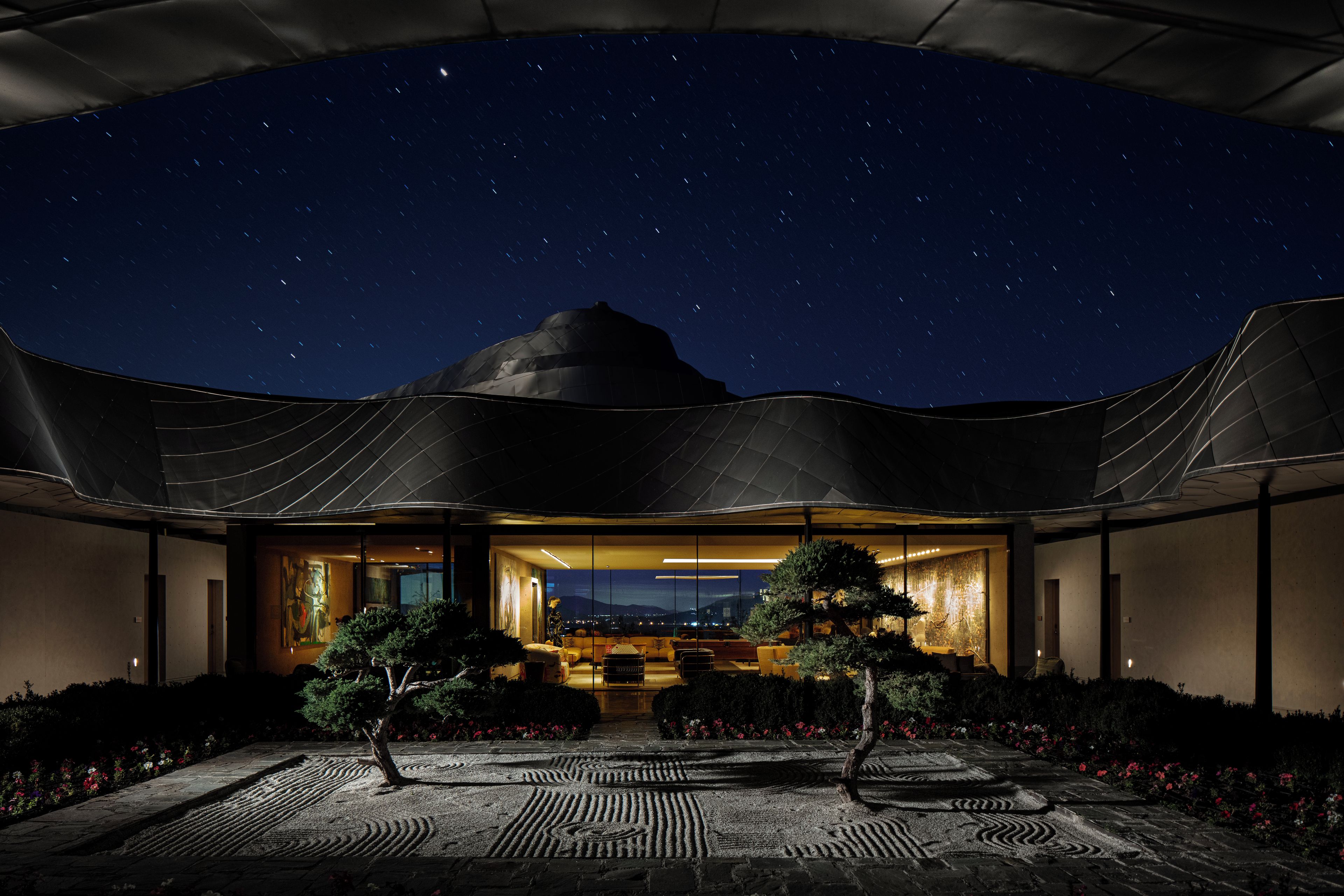 A modern building with a large glass facade, a covered outdoor area, and a starry night sky.