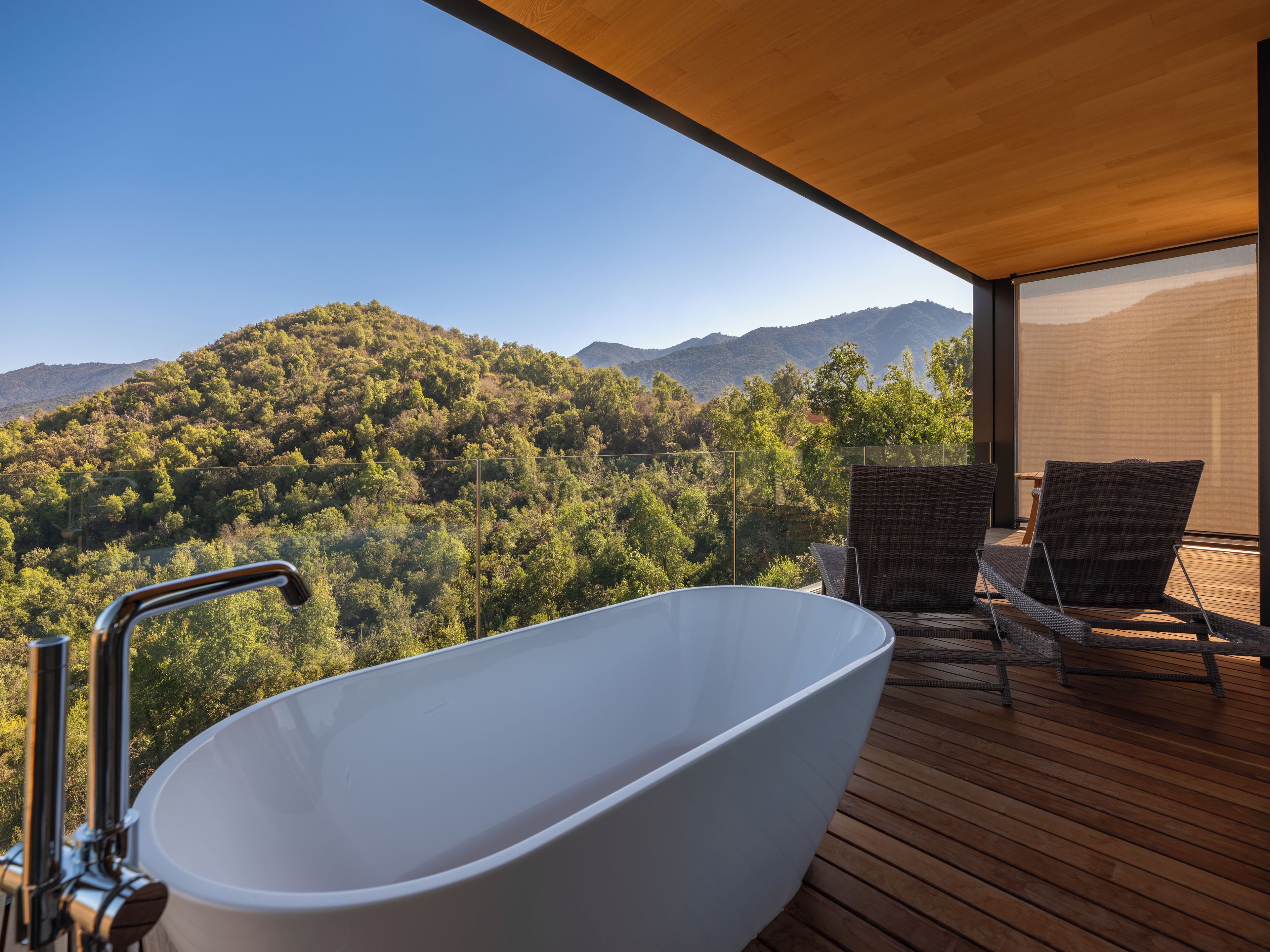 Une salle de bain moderne avec une baignoire sur pieds, une terrasse en bois et des fauteuils en osier.