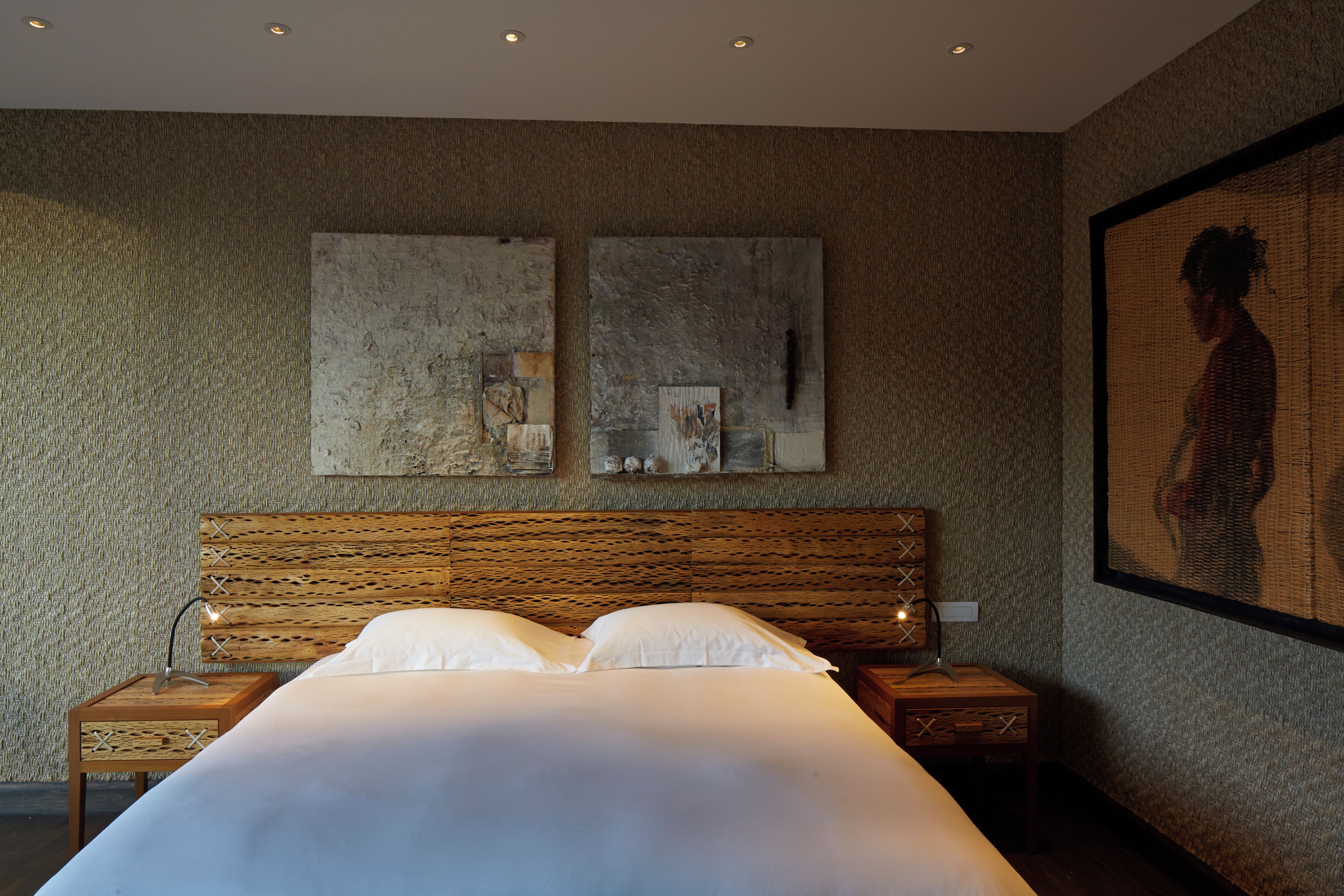 A bedroom with a large bed, wooden headboard, two bedside tables, and artwork on the walls.