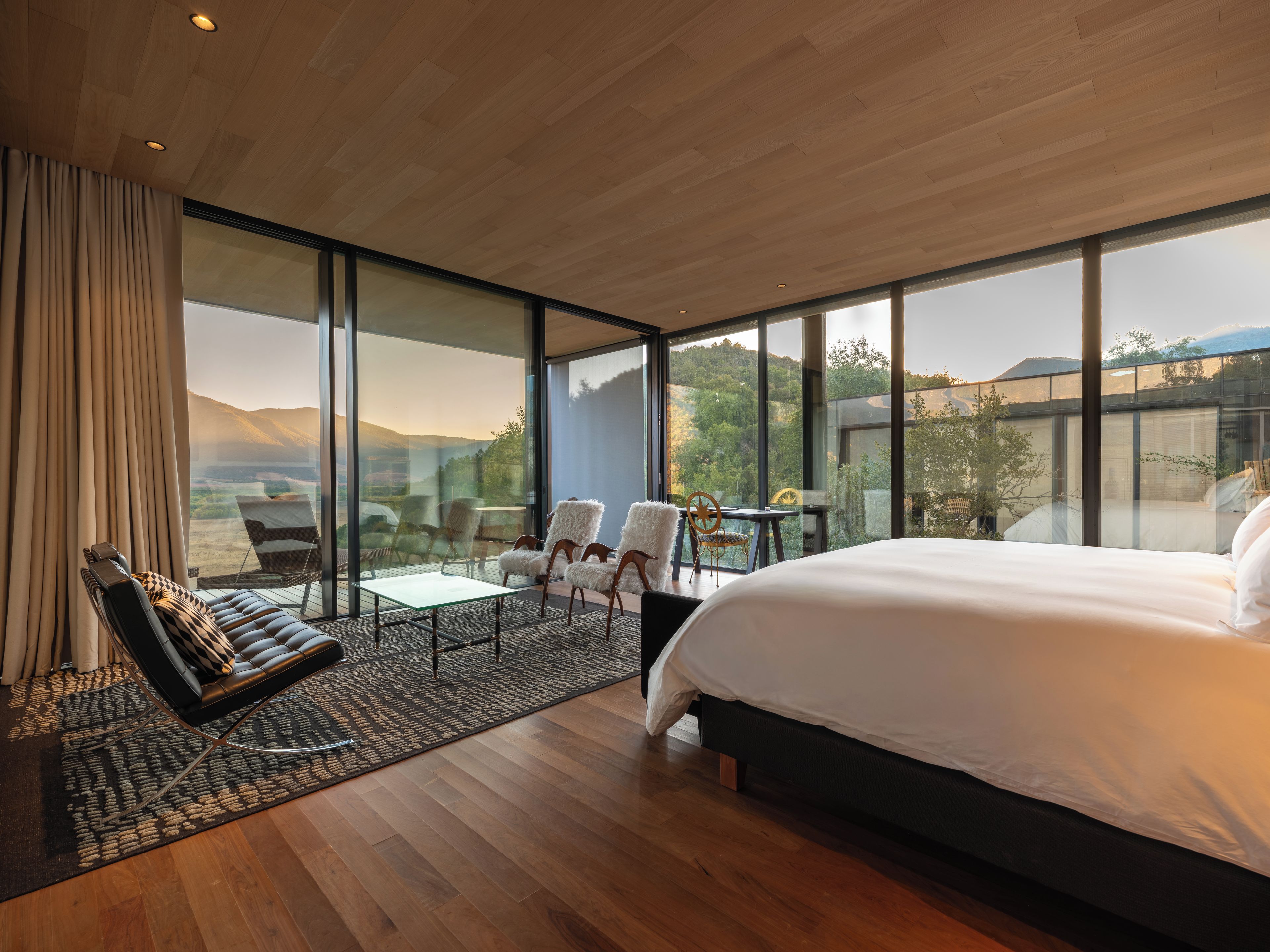 Un dormitorio moderno con una cama grande, un rincón de estar con sillas y vistas al exterior.