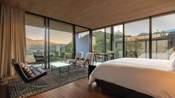Un dormitorio moderno con una cama grande, un rincón de estar con sillas y vistas al exterior.