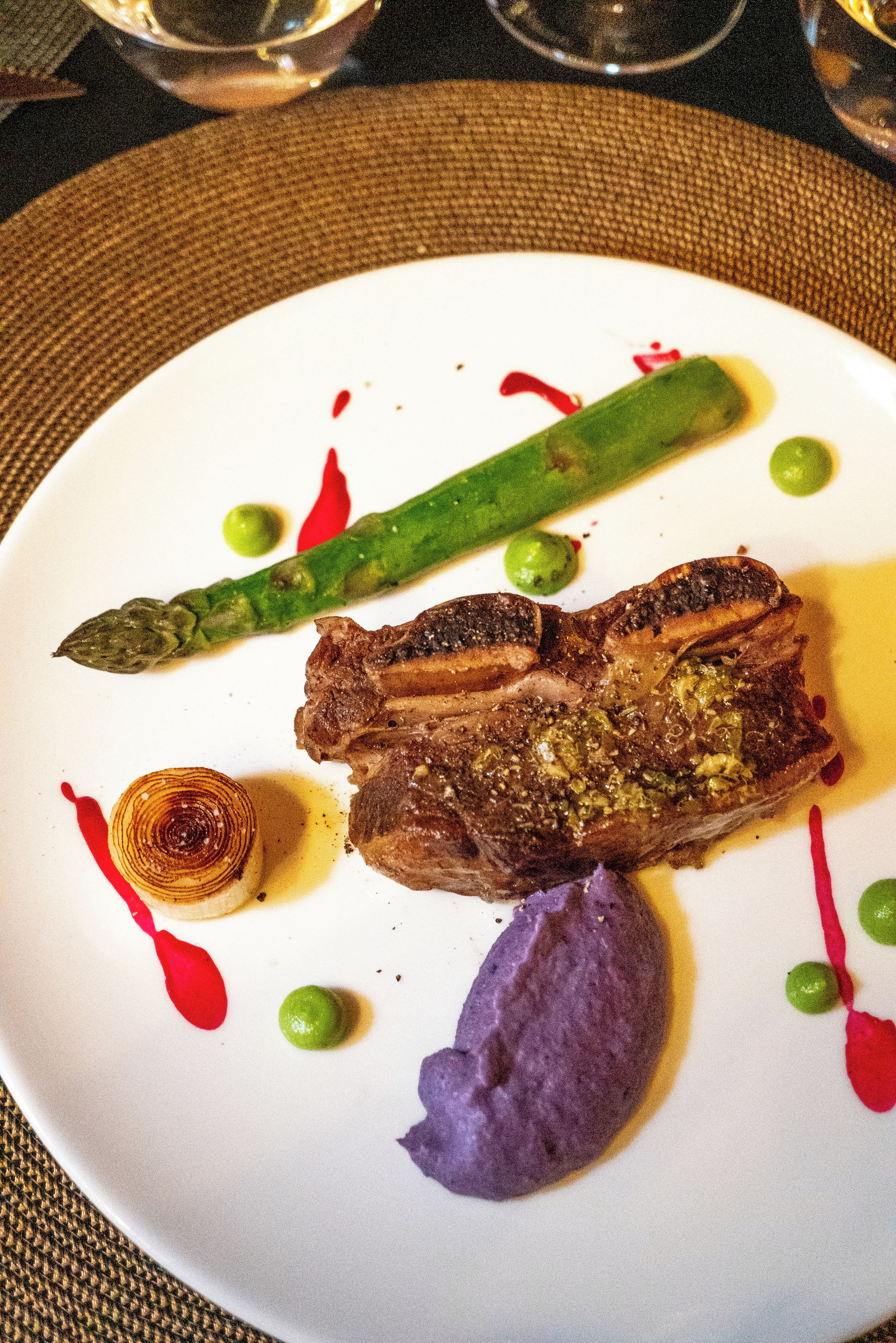 A plate with a steak, asparagus, and a purple vegetable, possibly a beetroot, with some sauce and a small onion ring.