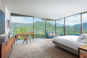 Un dormitorio con un ventanal grande, una cama, un escritorio con una silla y un sillón de peluche azul.