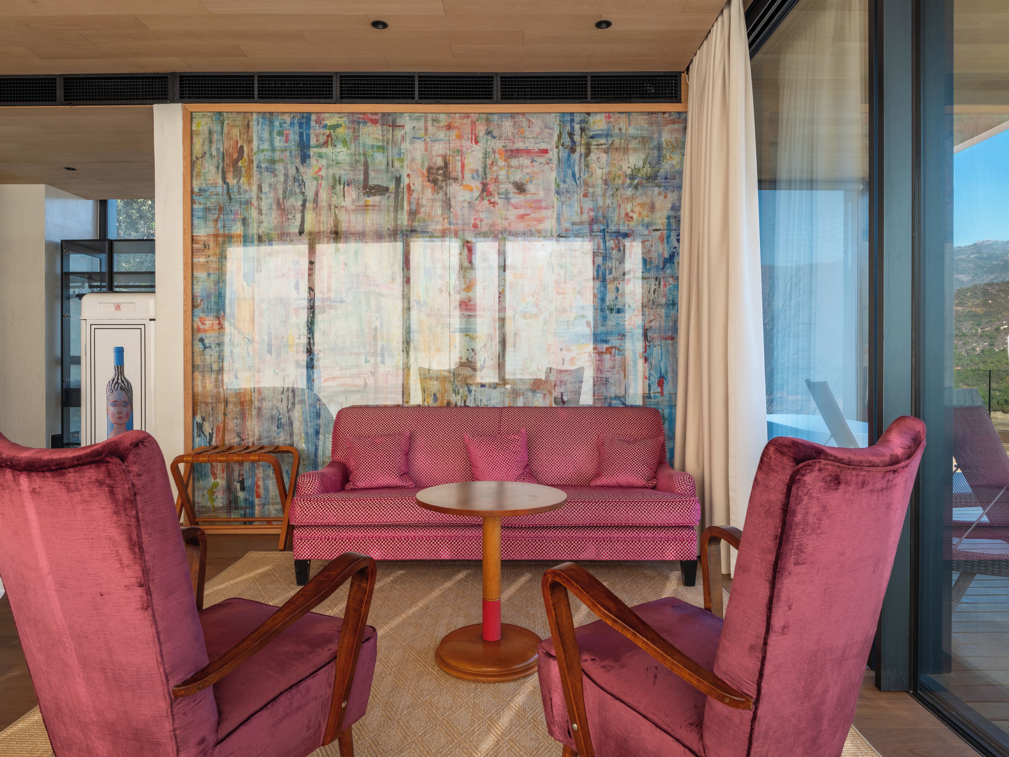En modern inredning med en röd soffa, två rosa fåtöljer och en stor, abstrakt tavla på väggen.