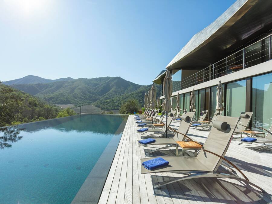 Zona junto a la piscina con sillones de descanso y vistas a montañas.