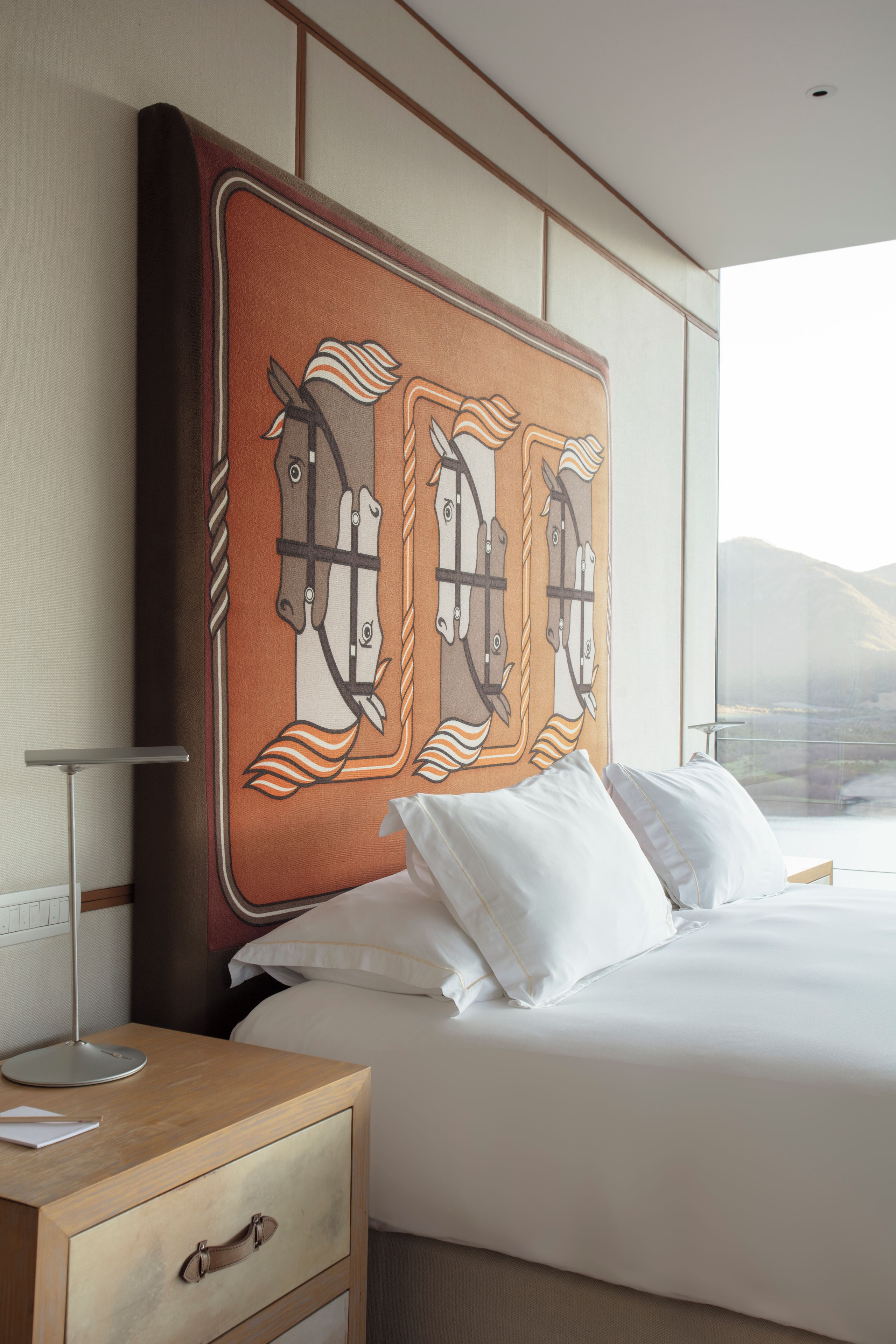 A hotel room with a large bed, a bedside table with a lamp, and a wall-mounted artwork of horses.