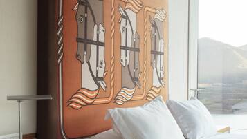 A hotel room with a large bed, a bedside table with a lamp, and a wall-mounted artwork of horses.
