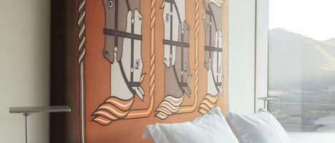 A hotel room with a large bed, a bedside table with a lamp, and a wall-mounted artwork of horses.