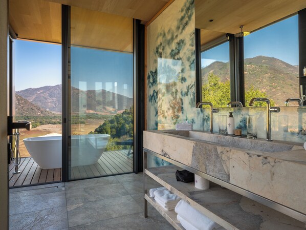 Un baño moderno con una bañera grande, una encimera de mármol y vistas a un paisaje montañoso.