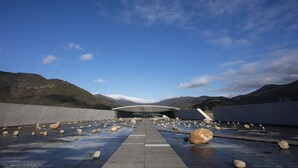 A modern building with a curved roof, surrounded by a rocky landscape and mountains.