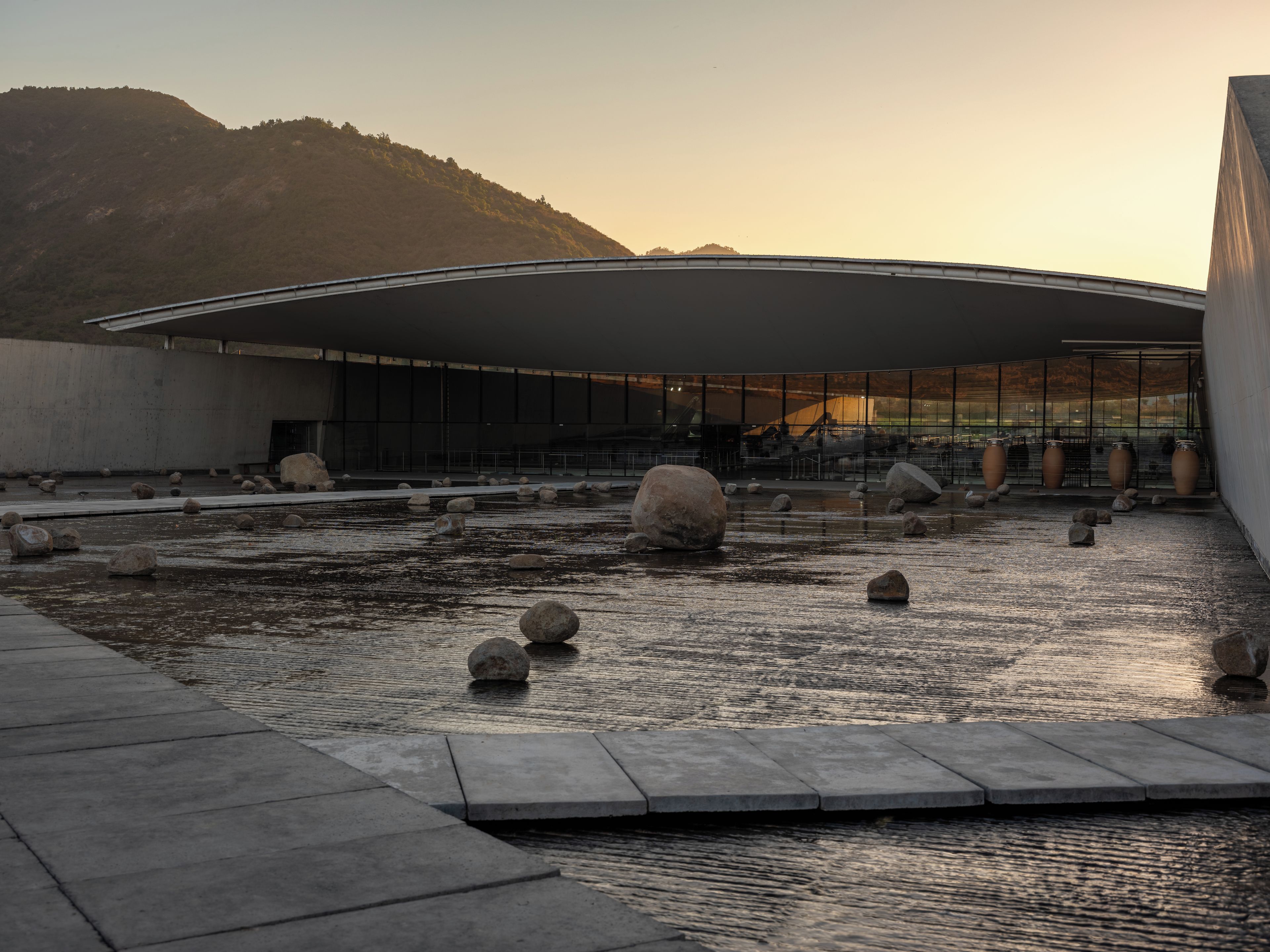 A modern building with a curved roof and a water feature with rocks.