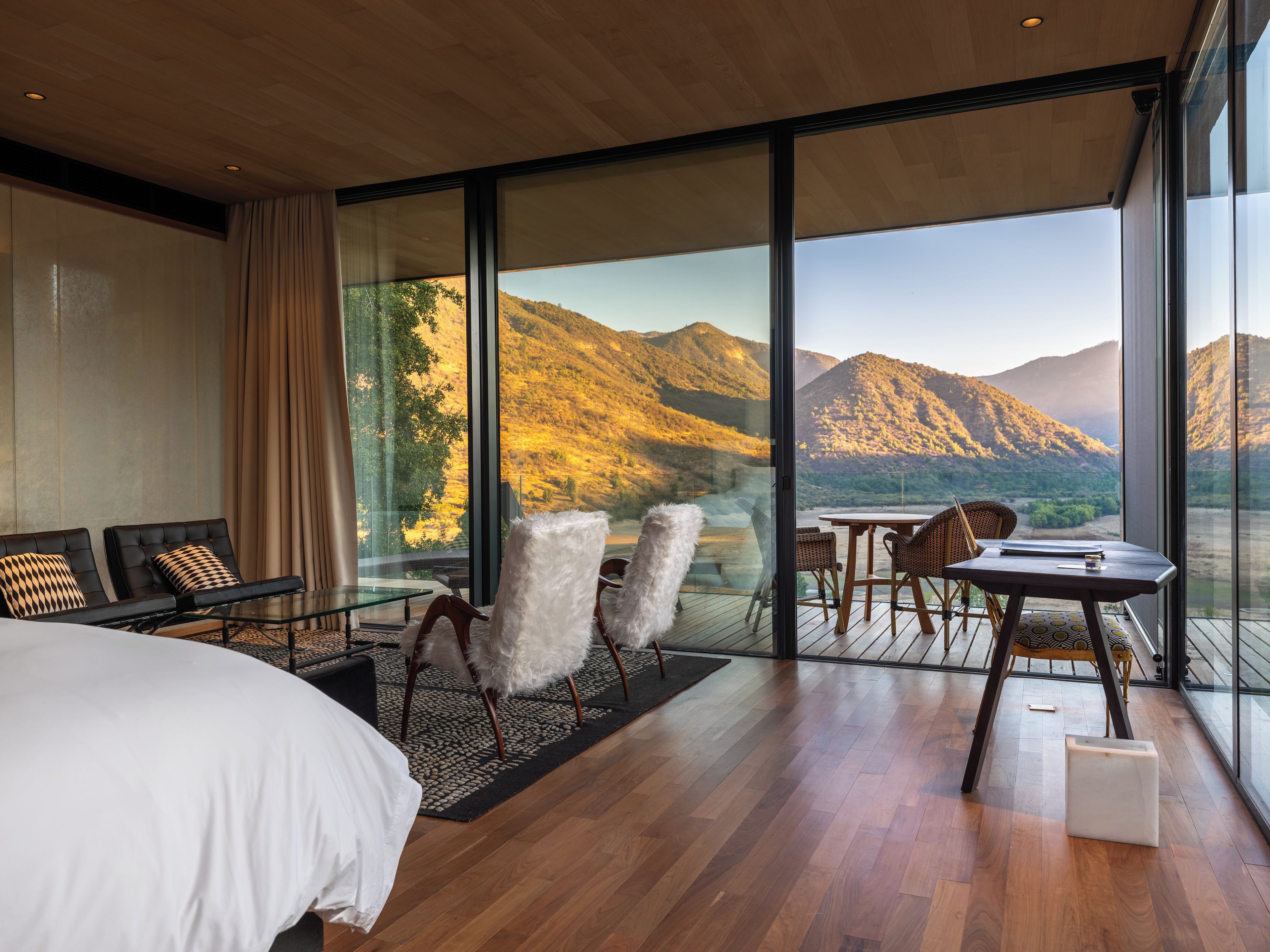 Una habitación de hotel moderna con un ventanal grande, una cama, una zona de estar con sillas y una mesita.