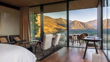 Una habitación de hotel moderna con un ventanal grande, una cama, una zona de estar con sillas y una mesita.