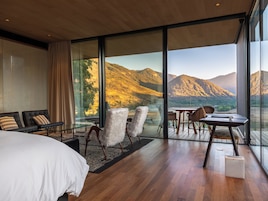Una habitación de hotel moderna con un ventanal grande, una cama, una zona de estar con sillas y una mesita.