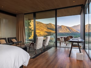 A modern hotel room with a large window, a bed, a seating area with chairs, and a small table. - Vik Chile (San Vicente)
