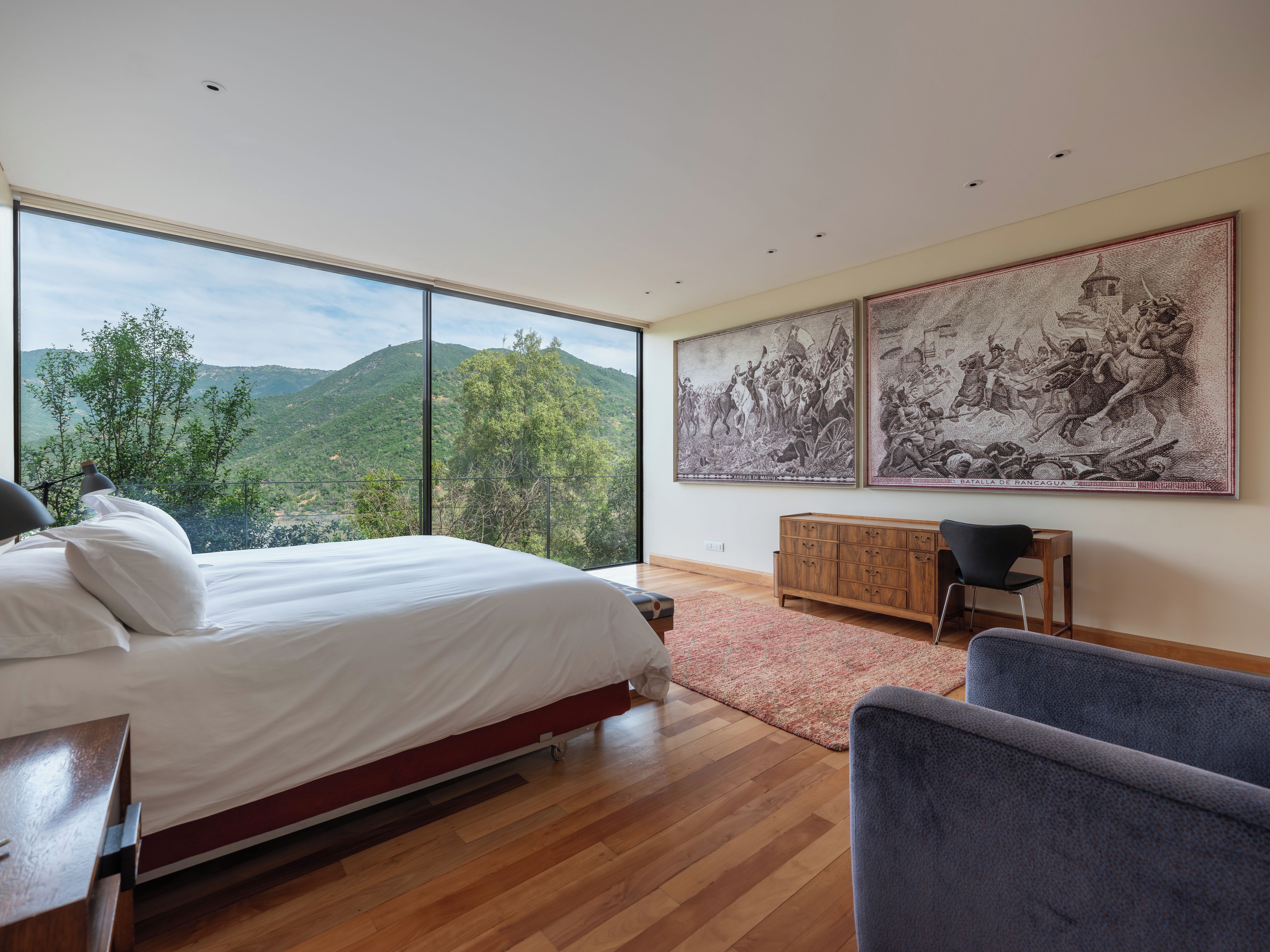 Un dormitorio con una cama grande, un escritorio y dos sillas. Hay dos cuadros grandes en la pared.