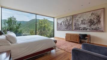 Un dormitorio con una cama grande, un escritorio y dos sillas. Hay dos cuadros grandes en la pared.