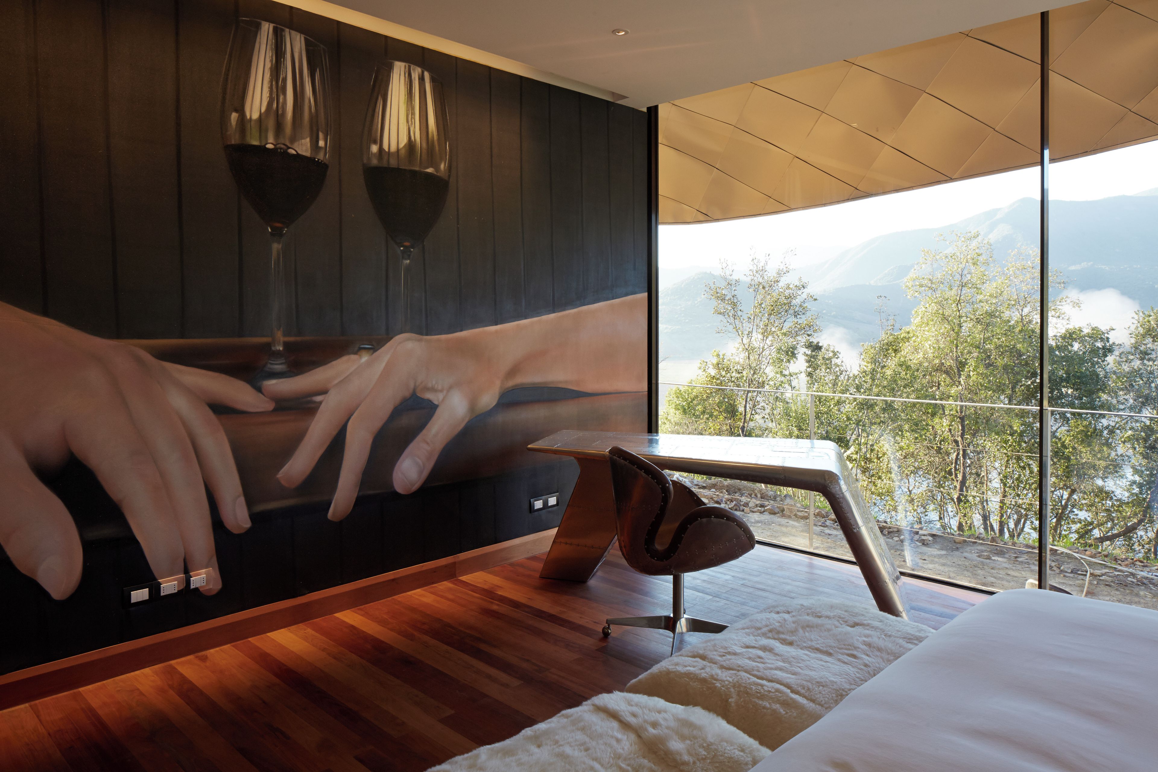 A bedroom with a large window, a bed, a wooden floor, and a wall-mounted artwork.
