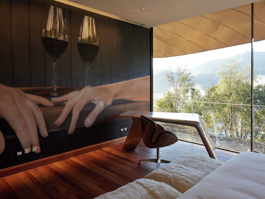 A bedroom with a large window, a bed, a wooden floor, and a wall-mounted artwork.