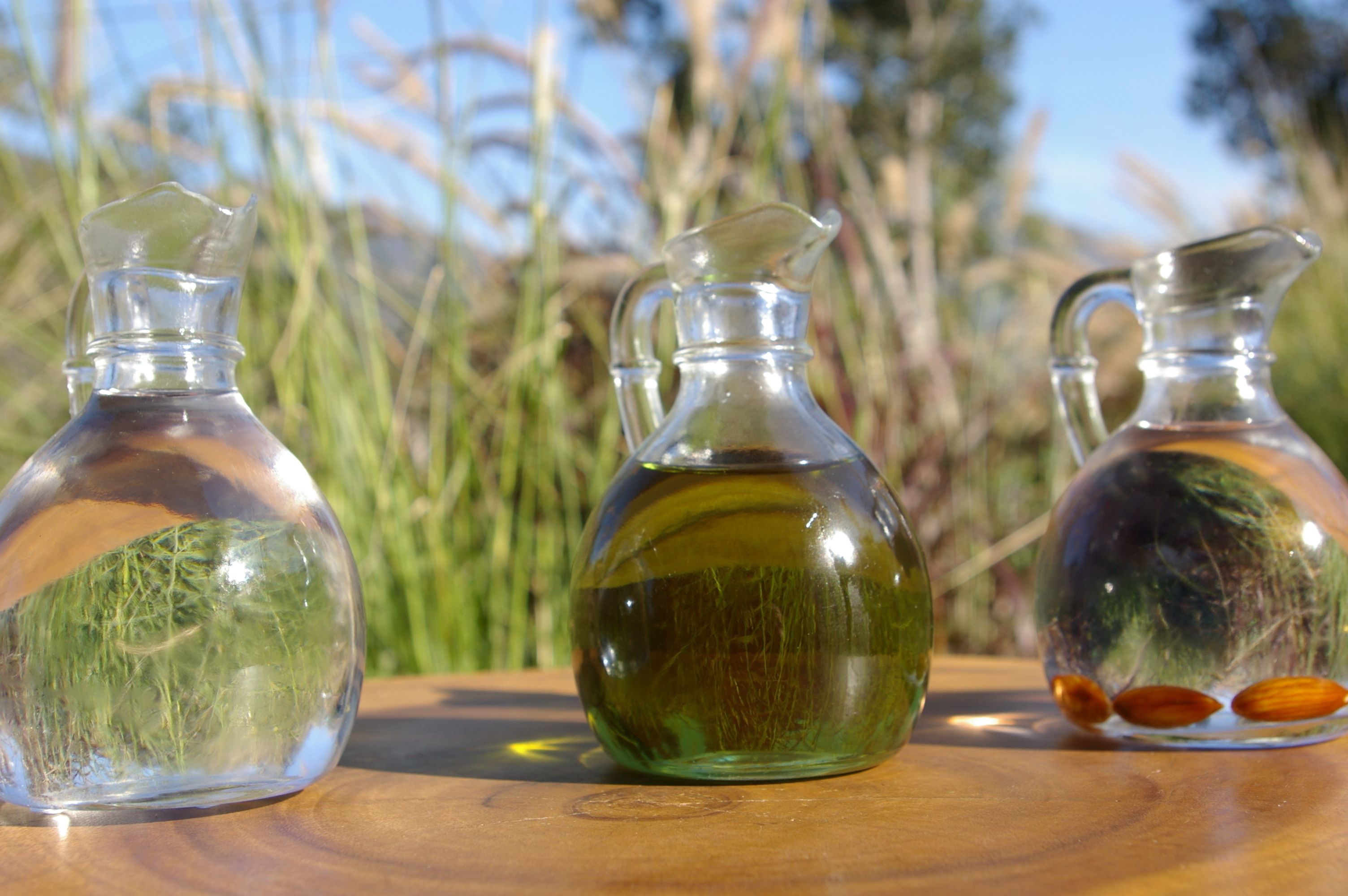 Trois bouteilles en verre, contenant chacune un liquide différent, sont posées sur une surface en bois.