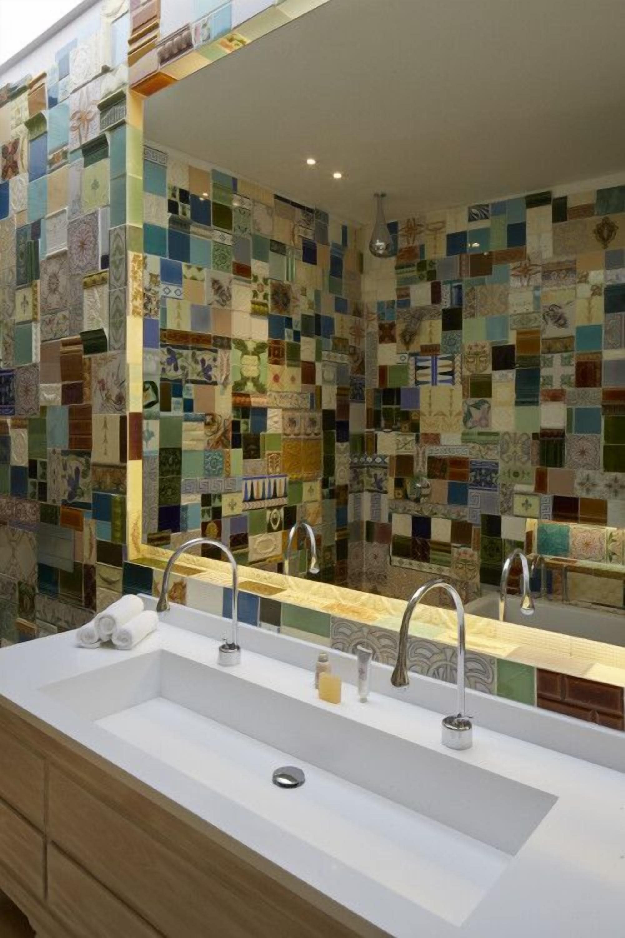 A bathroom with a tiled mosaic wall, a white sink with two faucets, and a mirror above the sink.