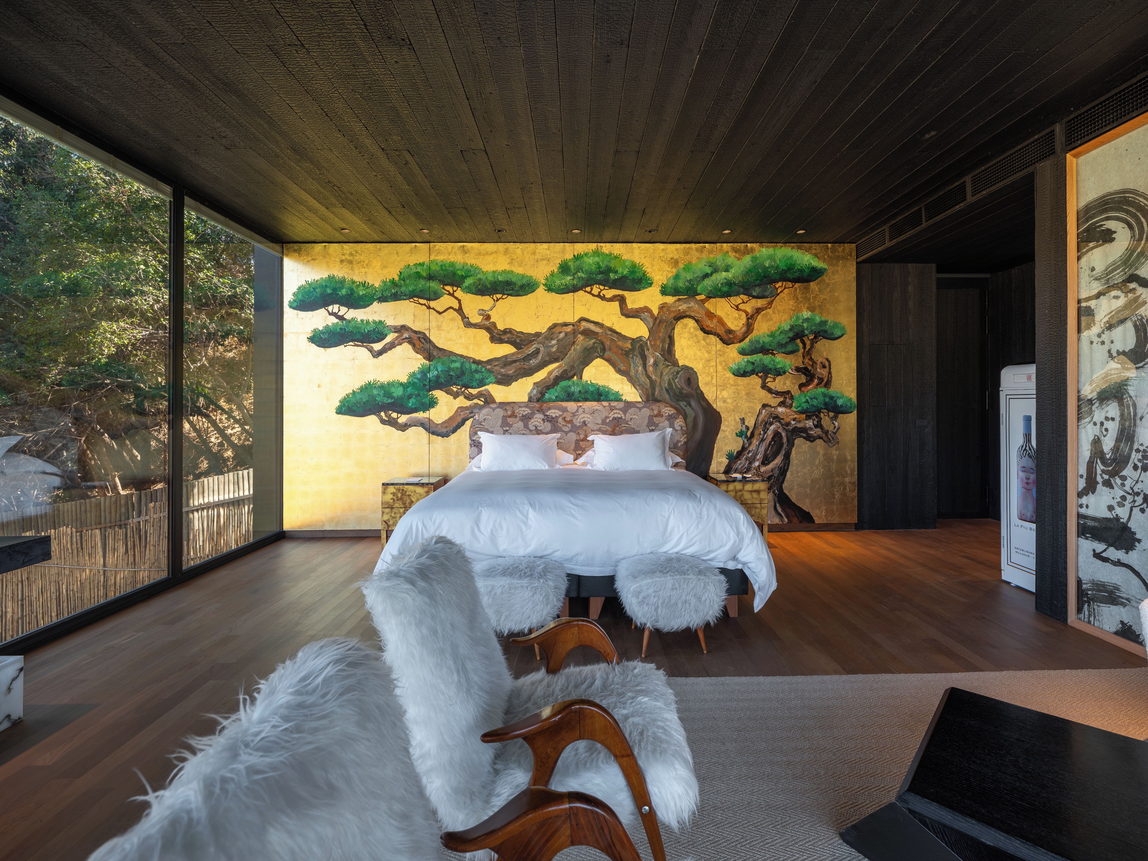 Une chambre avec un grand lit, un plafond en bois et une fresque murale représentant des arbres.