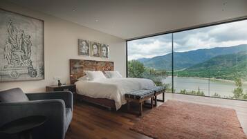 Un dormitorio con una cama grande, un escritorio, una silla y vistas a un lago y montañas.