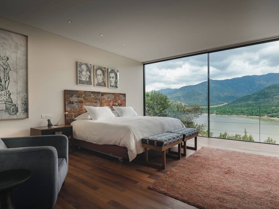 A bedroom with a large bed, a desk, a chair, and a view of a lake and mountains.