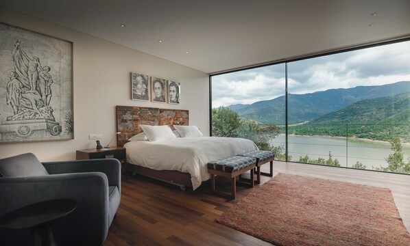 Un dormitorio con una cama grande, un escritorio, una silla y vistas a un lago y montañas.