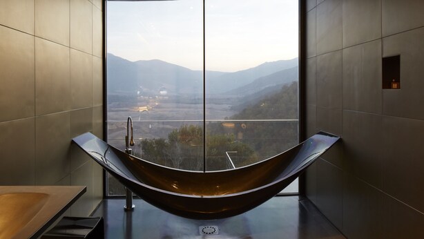 A modern bathroom with a large window, a curved bathtub, and a view of a valley.