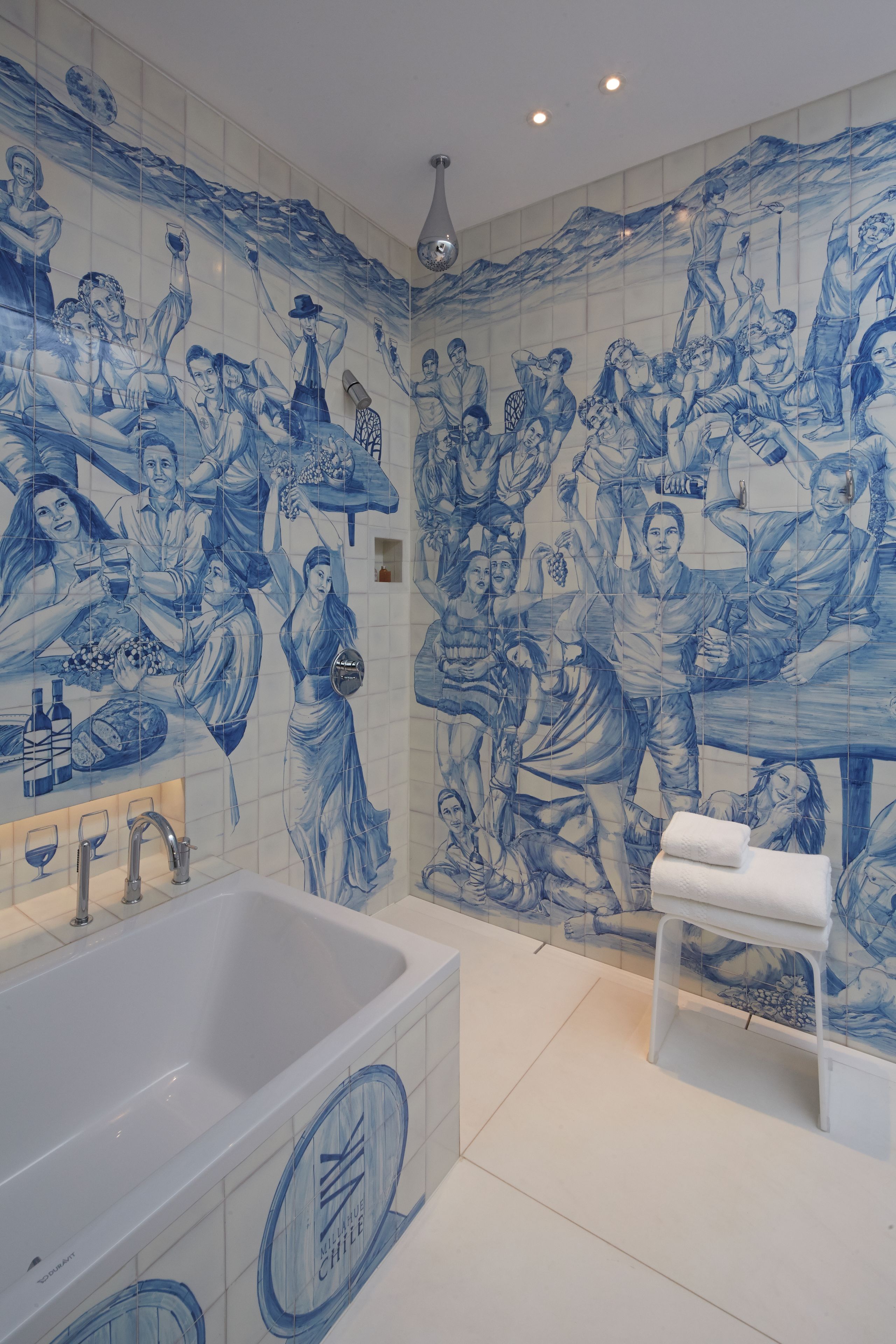 A bathroom with a large bathtub, a shower area, and a wall with blue tile artwork depicting people.