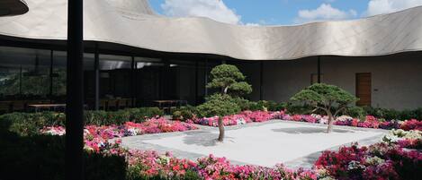 Un edificio moderno con techo curvo, un patio central lleno de flores coloridas y un área de comedor con mesas y sillas.
