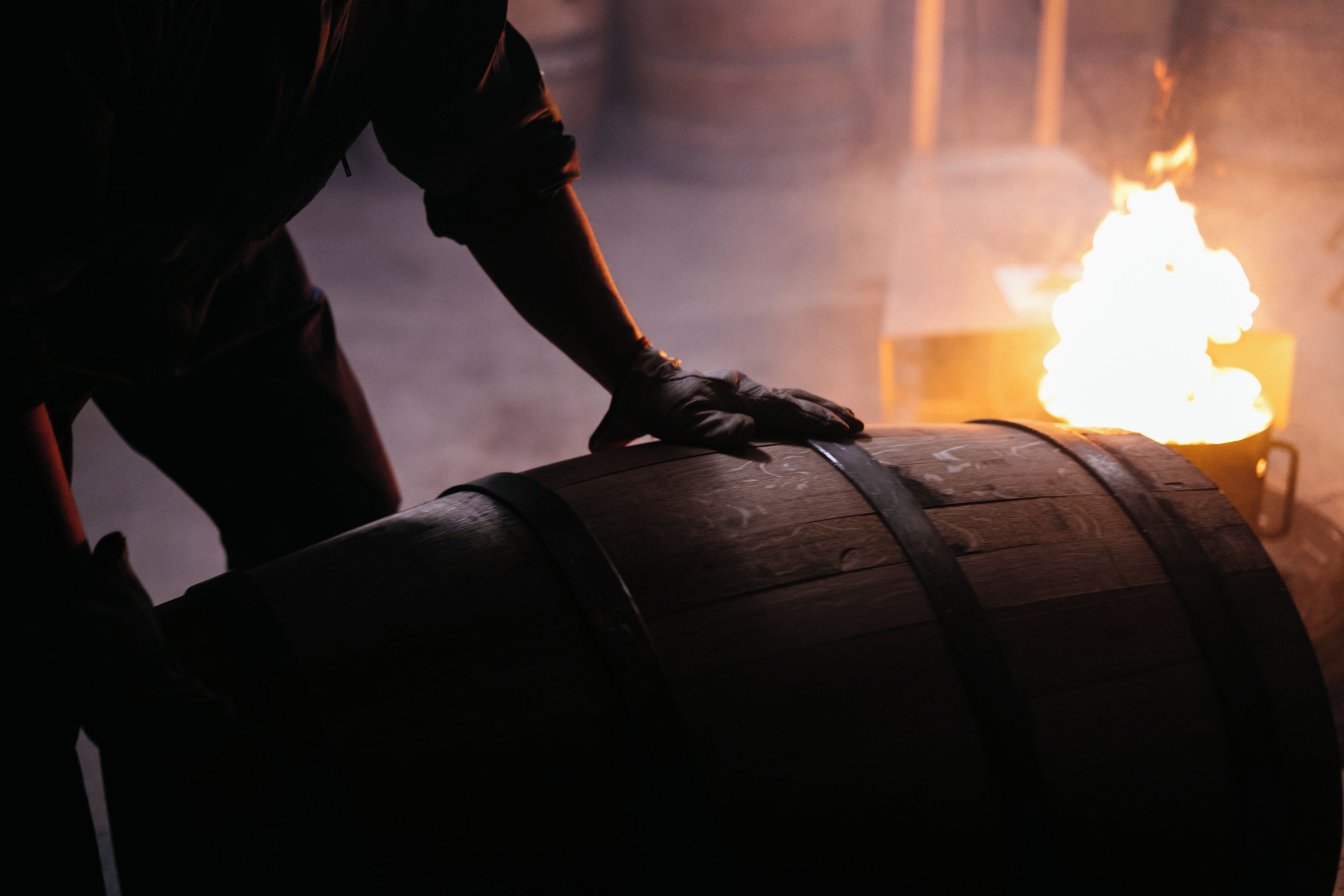 A person handling a wooden barrel with a strap, in a dimly lit environment with a visible flame.