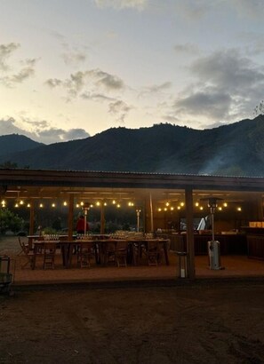 An outdoor dining area with tables and chairs, a covered seating area, and a view of mountains in the background. - Vik Chile (San Vicente)
