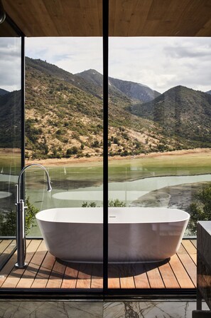 A modern bathroom with a freestanding bathtub, a glass-enclosed shower, and a view of a mountainous landscape.