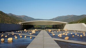 A modern building with a curved roof and a pathway leading to it, surrounded by large rocks and mountains in the background.