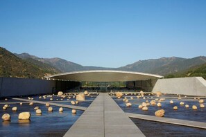 A modern building with a curved roof and a pathway leading to it, surrounded by large rocks and mountains in the background.