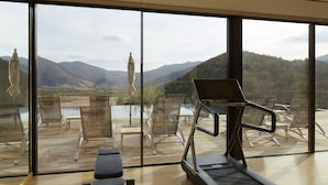 A modern room with large windows, a treadmill, and a view of a lake and mountains.
