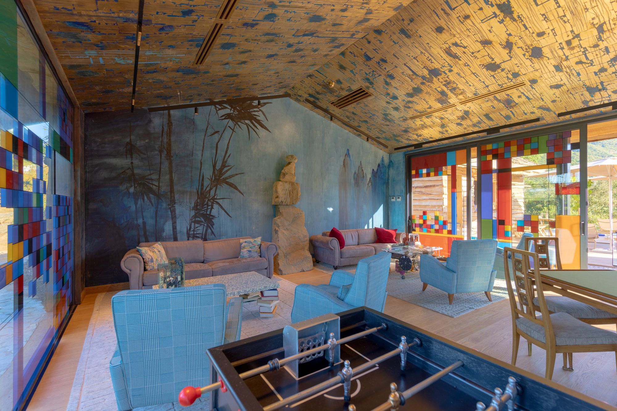 A room with a foosball table, sofas, and a large window with colorful view blocks.