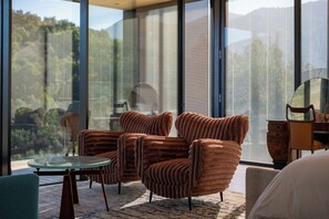 Un interior moderno con un sofá, una mesa de vidrio y vistas a un bosque a través de grandes ventanales.
