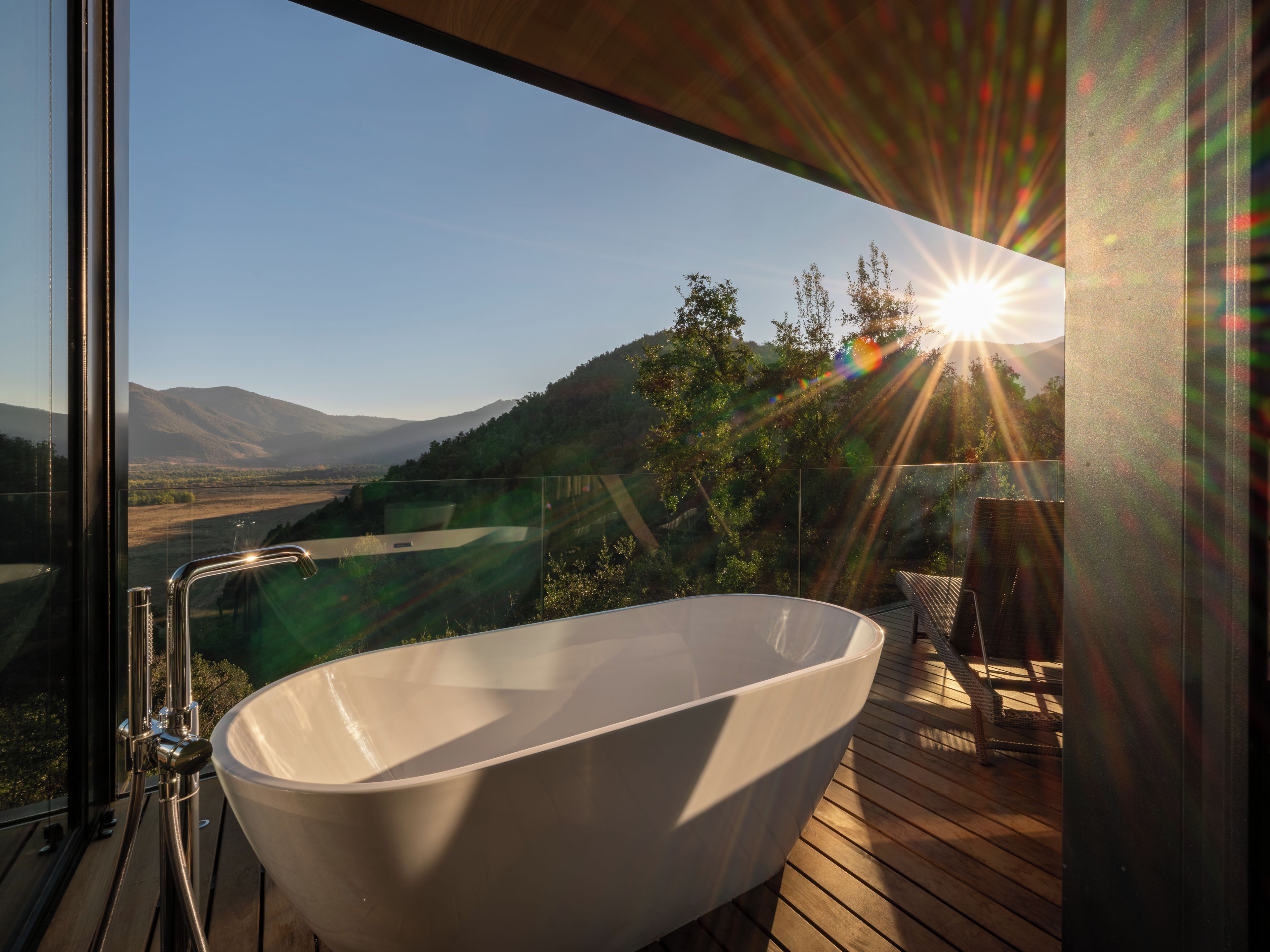 A modern bathroom with a freestanding bathtub, a glass-enclosed shower, and a view of a mountainous landscape.